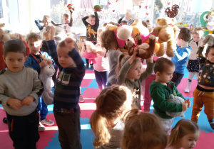Widok na salę przedszkolną. Przedszkolaki tańczą ze swoimi misiami.