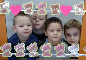 Widok na czterech chłopców, którzy pozują do zdjęcia stojąc za ramką ozdobioną misiami i różowymi serduszkami.