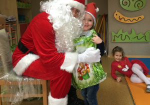 Widok na Św. Mikołaja i dziewczynkę, która przytula się do niego trzymając w ręku prezent.