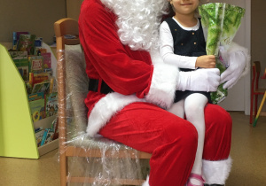 Dziewczyna siedzi na kolanach u Św. Mikołaja z otrzymanym prezentem.