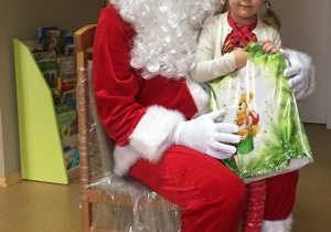 Dziewczyna siedzi na kolanach u Św. Mikołaja z otrzymanym prezentem.