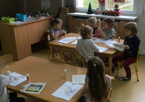 Widok na salę przedszkolną i przedszkolaków siedzących przy stolikach.
