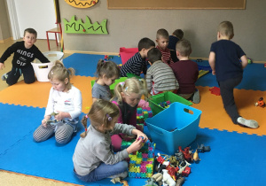 Dzieci siedzą na macie i bawią się wspólnie klockami i figurkami zwierząt.