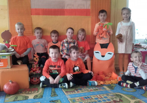 kolejna grupa dzieci w pomarańczowych ubraniach pozują do zdjęcia na pomarańćzowym tle.