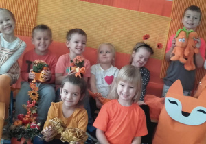 Dzieci w pomarańczowych ubraniach pozują do zdjęcia na pomarańćzowym tle.