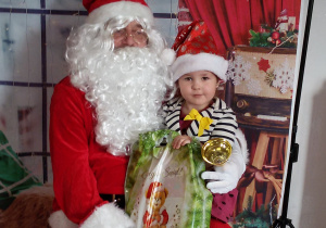 Dziecko siedzi na kolanach Świętego Mikołaja. W tle świąteczna dekoracja.