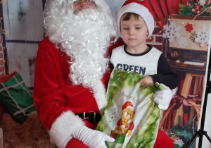 Dziecko siedzi na kolanach Świętego Mikołaja. W tle świąteczna dekoracja.