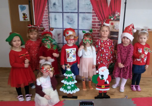 Dziewczynki w mikołajkowo- świątecznych strojach pozują do zdjęcia na tle świątecznej dekoracji.