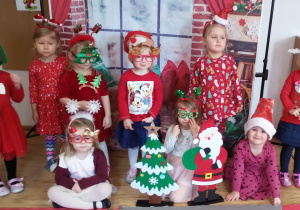 Dziewczynki w mikołajkowo- świątecznych strojach pozują do zdjęcia na tle świątecznej dekoracji.