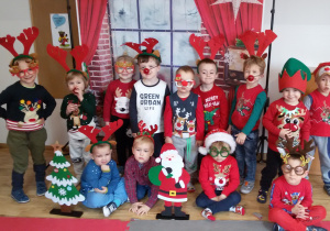 Chłopcy w mikołajkowo- świątecznych strojach pozują do zdjęcia na tle świątecznej dekoracji.