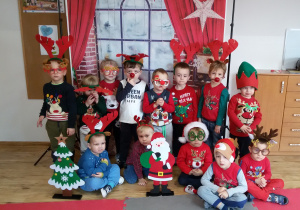 Chłopcy w mikołajkowo- świątecznych strojach pozują do zdjęcia na tle świątecznej dekoracji.
