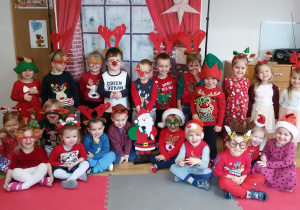 Zdjęcie grupowe. Dzieci w mikołajkowo- świątecznych strojach pozują do zdjęcia na tle dekoracji świątecznych.