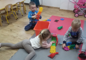 Widok na salę przedszkolną i dzieci, które bawią się klockami.