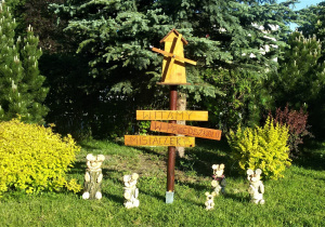 Widok na ogród przedszkolny, wykonane z tworzywa przyrodniczego misie i drewniany wiatrak, poniżej znajduje się napis: Witamy w przedszkolu Misiaczek.
